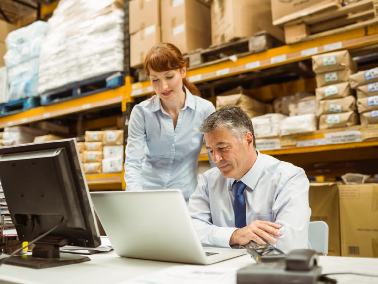 Warehouse management talking and looking at laptop in a large warehouse